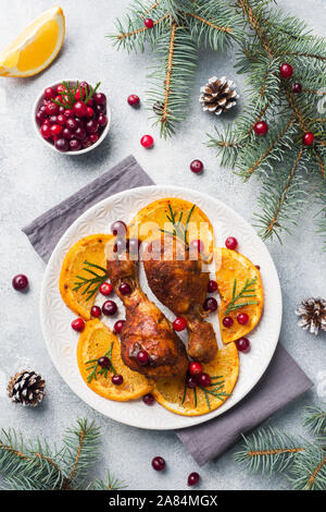 Baked chicken drumstick with oranges and cranberries in a plate light grey background. Christmas food Table with decorations Stock Photo