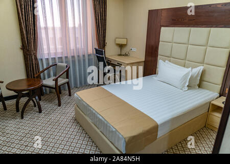 Hotel Comfortable Clean Double Bedroom with Beige Colored Curtain Linen and Table with Chairs Stock Photo