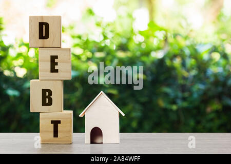 Conceptual about property debt. A small house model with stack of wooden block on nature background. Depicts debt resulting from the purchase of an ex Stock Photo