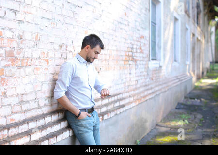 Handsome male man guy standing near wall and looking at watch on arm dressed. Stock Photo
