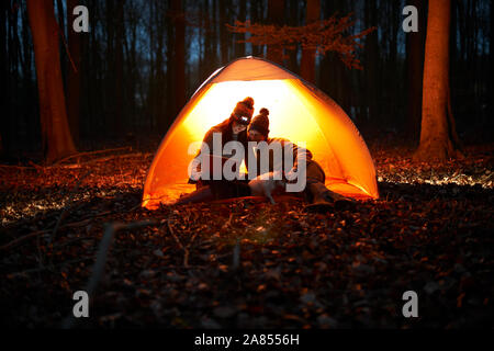 Couple using digital tablet inside glowing tent in woods at night Stock Photo