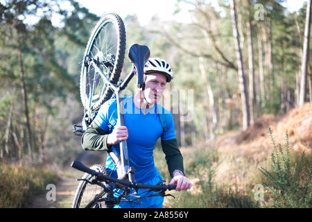 Male cyclist carrying bicycle on sunny trail in woods Stock Photo