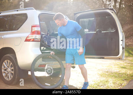 Male cyclist removing bike tire from back of SUV in sunny parking lot Stock Photo