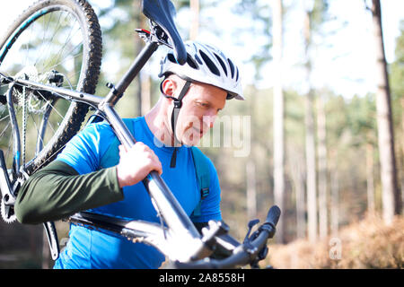 Male cyclist carrying bicycle in sunny woods Stock Photo