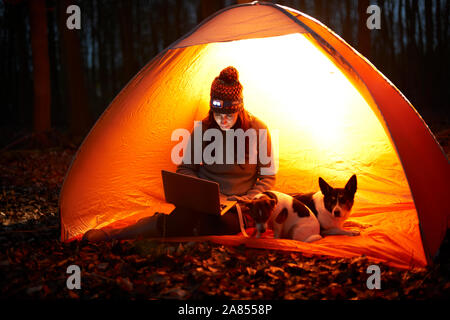 Woman with dog using laptop in glowing tent Stock Photo