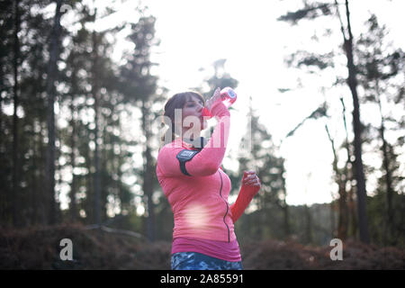 Female runner drinking from water bottle in woods Stock Photo
