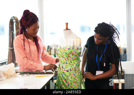 Female fashion designers pinning dress on dressmakers model in studio Stock Photo