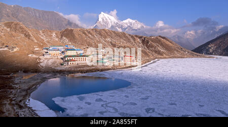 Spectacular panorama of the frozen Gokyo lake in the high Himalayan mountains; the same name village on the shore of a reservoir and snowy peaks tower Stock Photo