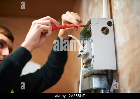 Male electrician using screwdriver, working at electric panel Stock Photo