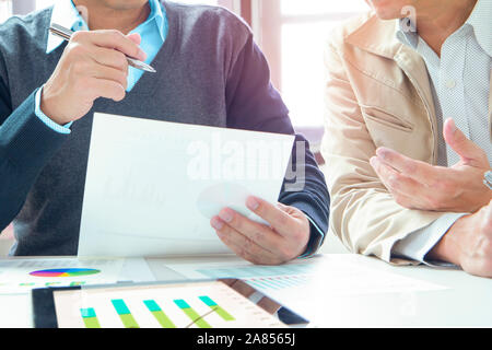 Two men discuss and express their idea in an office meeting room while reviewing financial reports for business performance. Stock Photo
