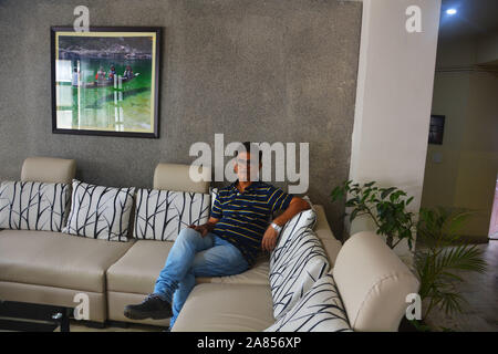 Man sitting on a sofa with cushions relaxing  and  a photograph hanging on the wall Stock Photo