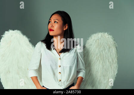 Serene, curious young woman wearing angel wings Stock Photo