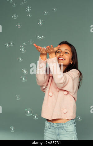 Smiling, carefree girl playing with falling bubbles Stock Photo