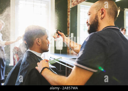 Male barber spraying hair of man in barbershop Stock Photo