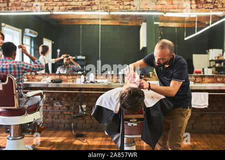 Male barber shaving face of customer in barbershop Stock Photo