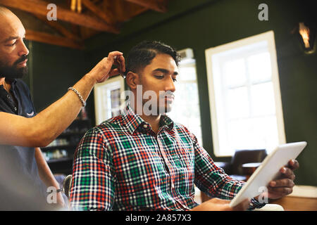 Man using digital tablet while receiving haircut in barbershop