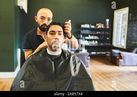 Male barber giving customer haircut in barbershop Stock Photo