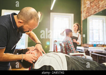 Male barber shaving face of customer in barbershop Stock Photo