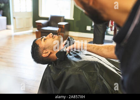 Male barber brushing face of customer in barbershop Stock Photo
