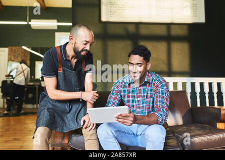 Male barber and customer using digital tablet in barbershop Stock Photo