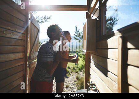 Father and son brushing teeth at sunny campsite bathroom sink Stock Photo