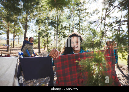 Smiling woman hanging clothing on campsite clothesline in woods Stock Photo