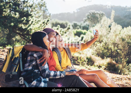 Happy mother and daughters taking selfie, hiking in sunny woods Stock Photo