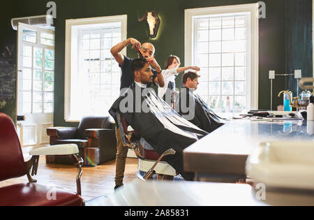 Male barber cutting hair of customer in barbershop