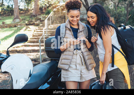 Young women friends using smart phone at motor scooter Stock Photo