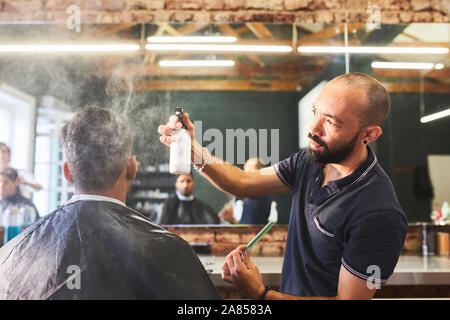 Male barber spraying hair of customer in barbershop