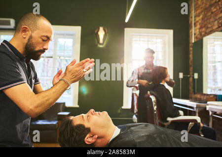 Male barber standing over customer in barbershop Stock Photo