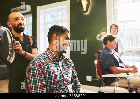 Male barber holding mirror for smiling customer in barbershop Stock Photo