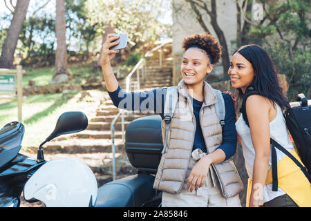 Happy young women friends taking selfie with camera phone at motor scooter Stock Photo
