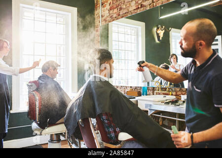 Male barber spraying hair of customer in barbershop Stock Photo