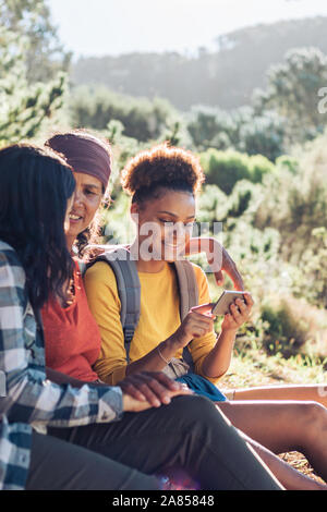 Mother and daughters using smart phone, hiking in sunny woods Stock Photo