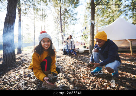 Portrait smiling girl gathering kindling at sunny campsite in woods Stock Photo