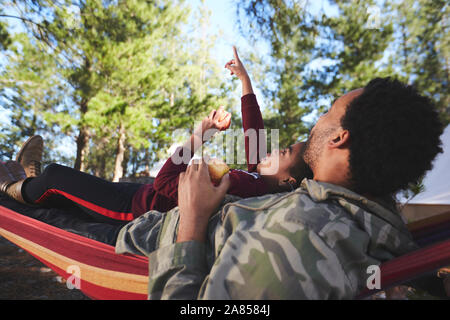 Father and son relaxing in hammock below trees in woods