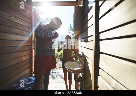 Father and son brushing teeth in sunny campsite bathroom Stock Photo