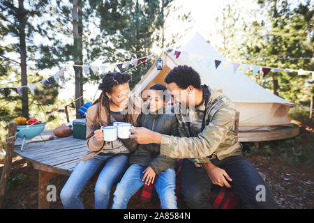 Happy family drinking coffee and hot chocolate at campsite in woods Stock Photo