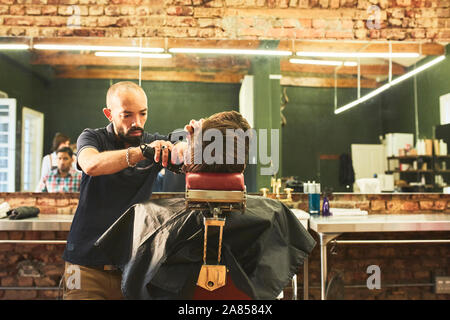 Male barber giving customer a haircut in barbershop - Stock Image