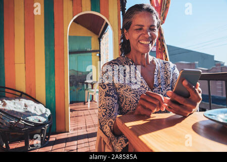 Smiling, happy woman using smart phone on sunny restaurant balcony Stock Photo