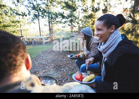 Happy friends eating at campsite in woods Stock Photo