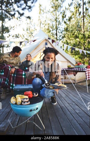 Smiling woman cooking vegetables on campsite grill Stock Photo
