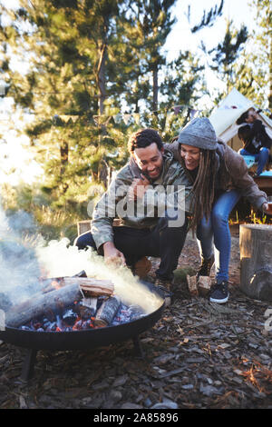 Happy couple tending to campfire at campsite in woods Stock Photo