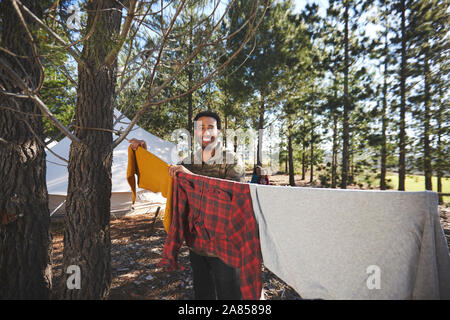 Portrait happy man hanging laundry on campsite clothesline n woods Stock Photo