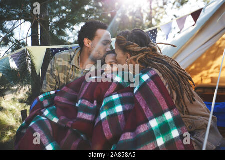 Happy, affectionate parents kissing son, relaxing at campsite Stock Photo
