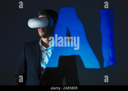 Double exposure businessman with virtual reality simulator glasses against AI text Stock Photo