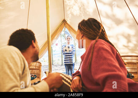 Couple watching son with soccer ball at camping yurt doorway Stock Photo