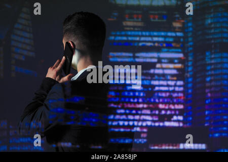 Double exposure businessman talking on smart phone against highrise lights at night Stock Photo