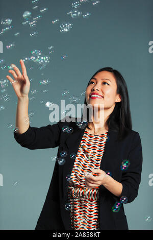 Portrait happy, playful businesswoman watching falling bubbles Stock Photo